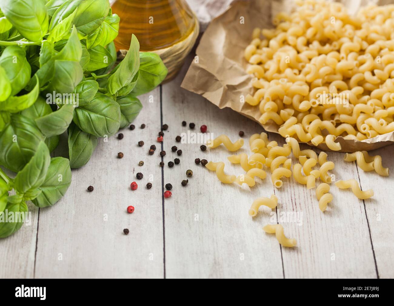 Maccheroni elbows classic raw pasta in brown paper on light wooden table background with basil and oil. Stock Photo