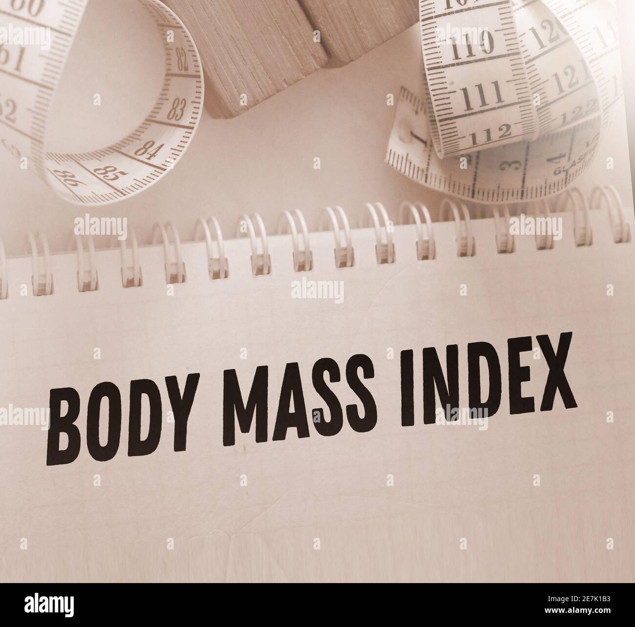 A white measuring tape and copybook with BMI body mass index words