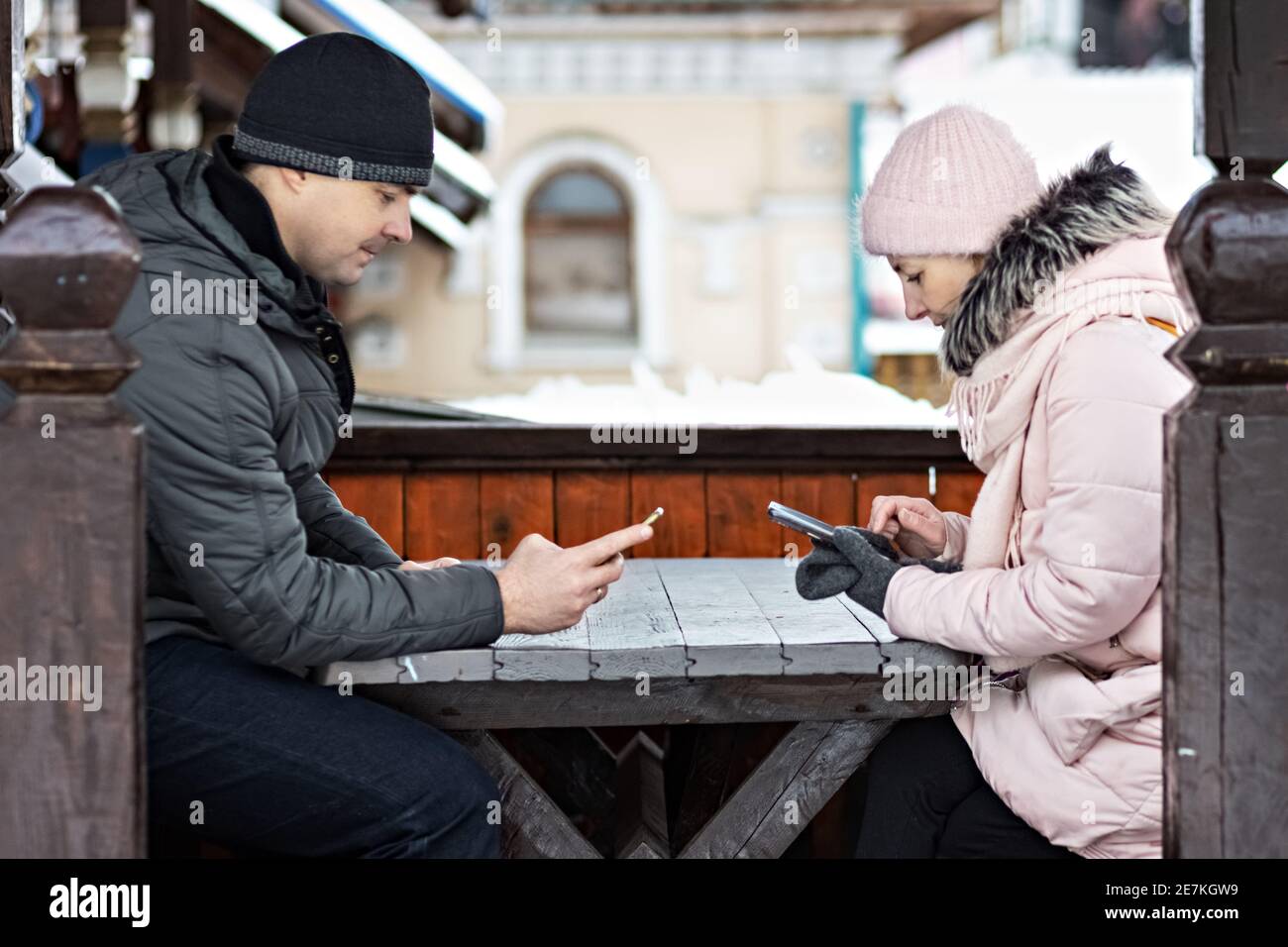 A couple is waiting for their order for lunch in a street cafe, texting by phone. Communication with people on a smartphone Stock Photo