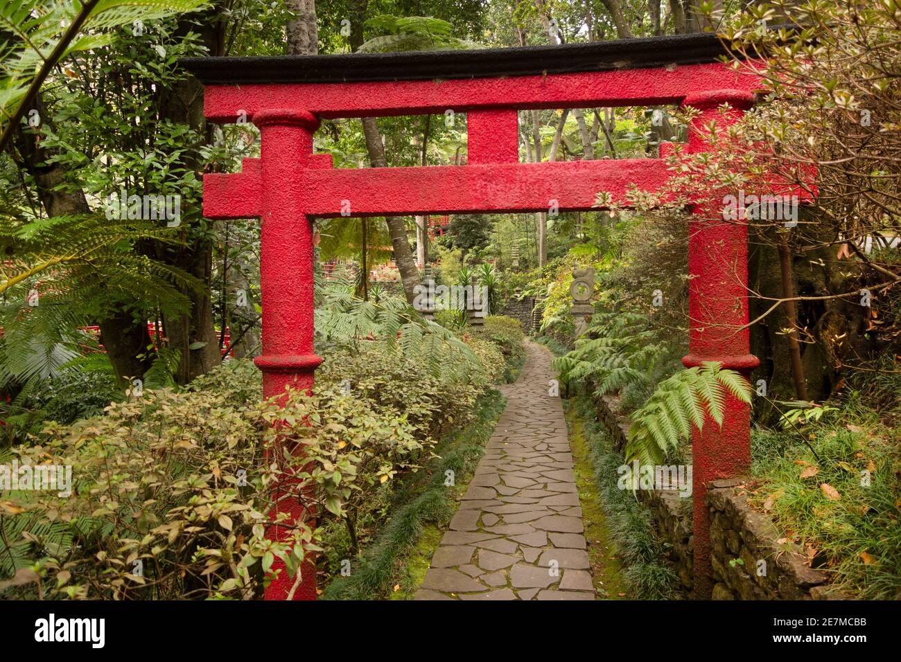 Red Oriental arch leading down a crazy paving path in the Northern Oriental Garden at Monte Palace Tropical Garden Stock Photo