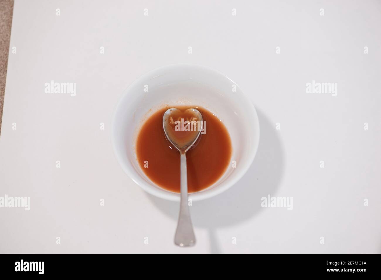 A heart-shaped spoonful of tomato alphabet soup spells out 'LOVE'. Studio set up on white. Stock Photo