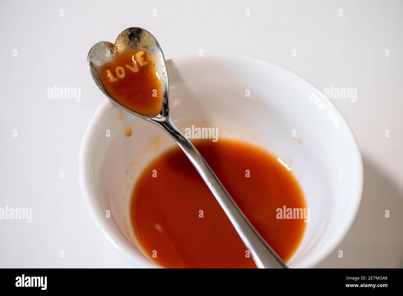 A heart-shaped spoonful of tomato alphabet soup spells out 'LOVE'. Studio set up on white. Stock Photo