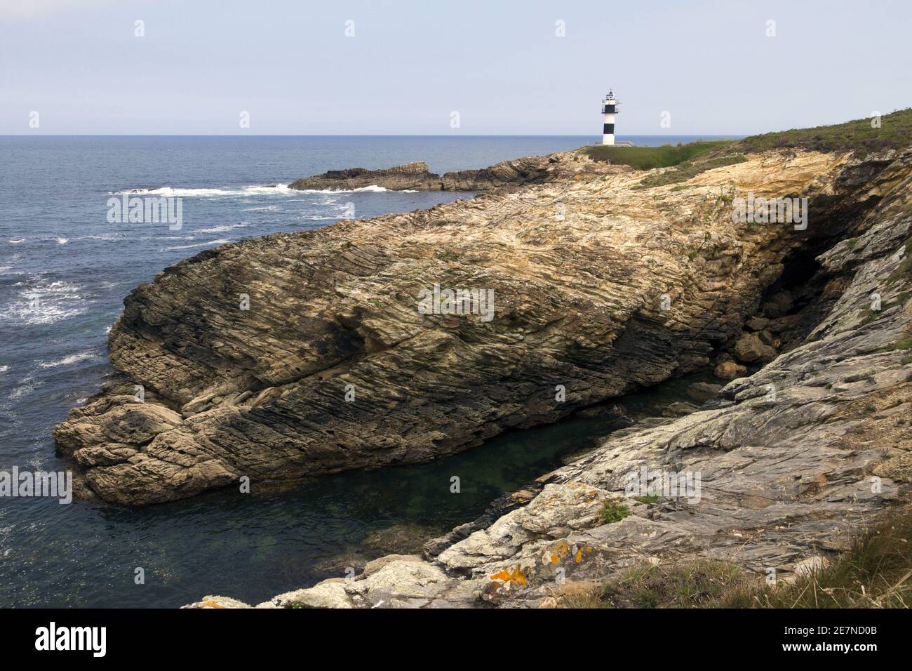 Rocks on the shore with the blue sea and a lighthouse Stock Photo