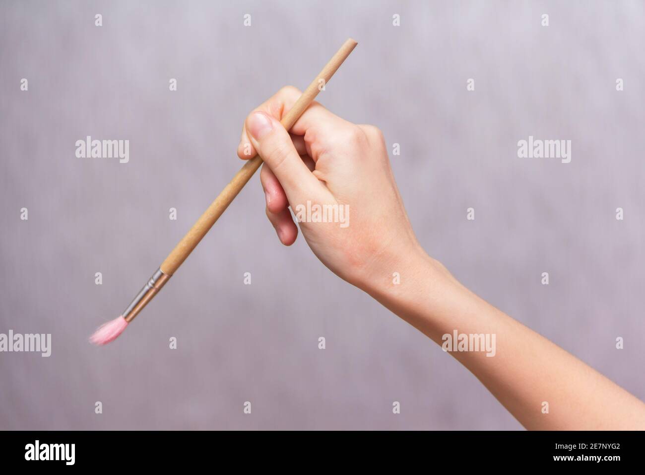 Girl's hand holding paint brush isolated on gray background ...
