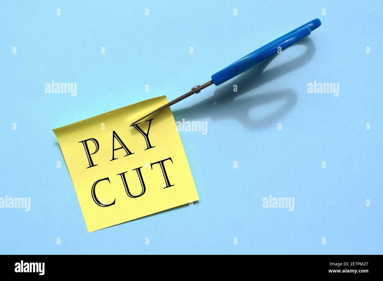 Scissors that cut yellow notepad with text on a blue background. Business concepts, cutting salary Stock Photo