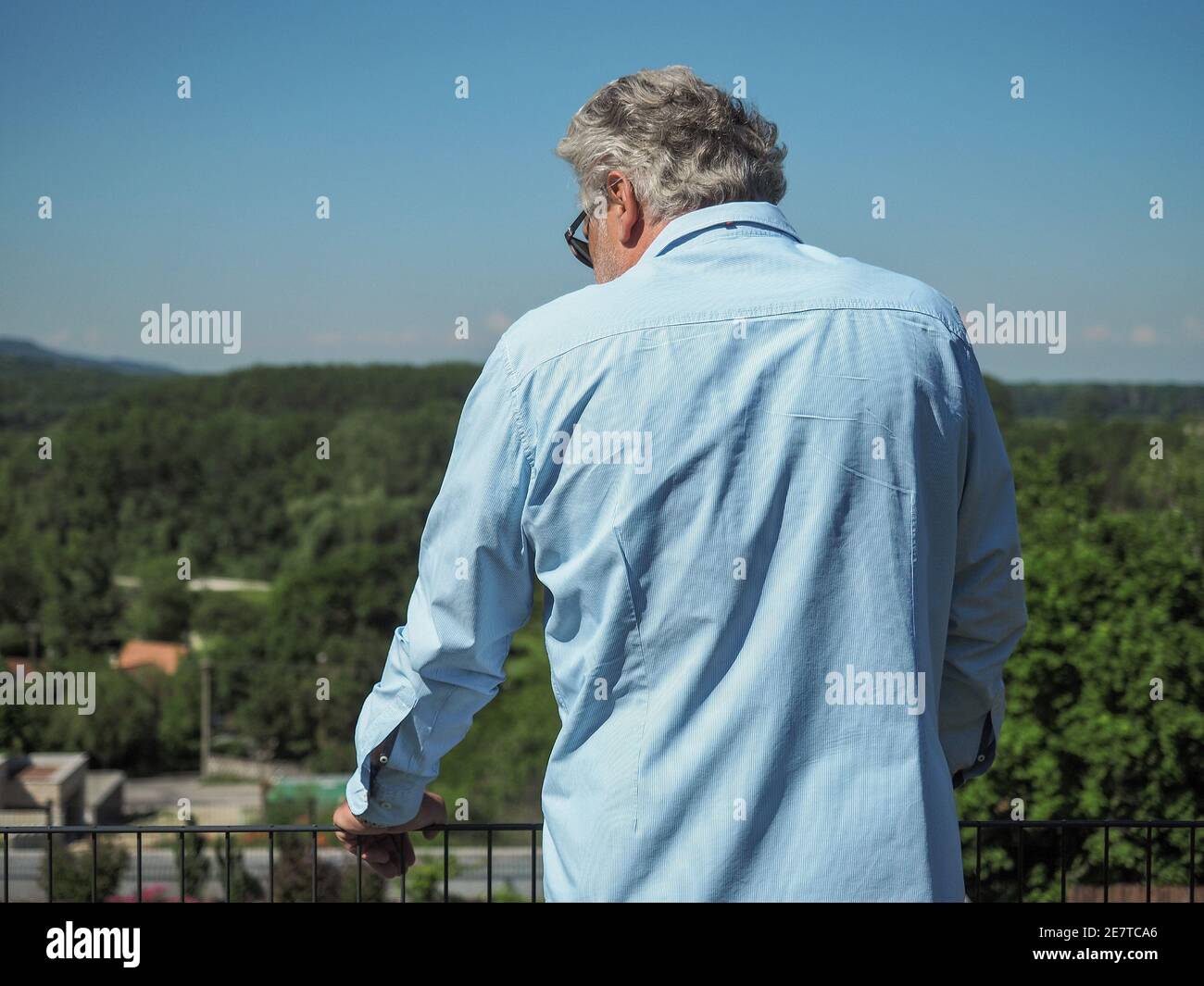 Senior man with grey hair stays in garden and looks on horizon. From behind. Mental health concept.  Stock Photo