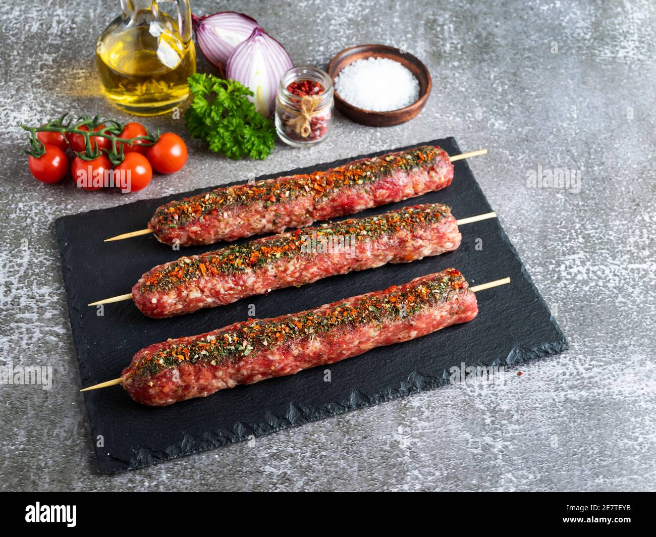 lula kebab raw meat wooden skewer on a black stone surface, spices Stock Photo