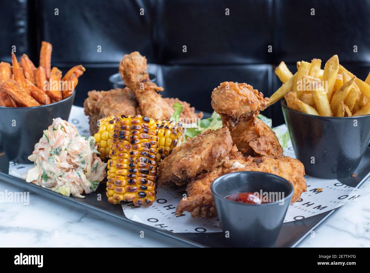 Sheffield, UK - 03 Aug 2017: Southern fried chicken and fries share platter with coleslaw and corn on the cob at OHM, Fitzwilliam Street Stock Photo