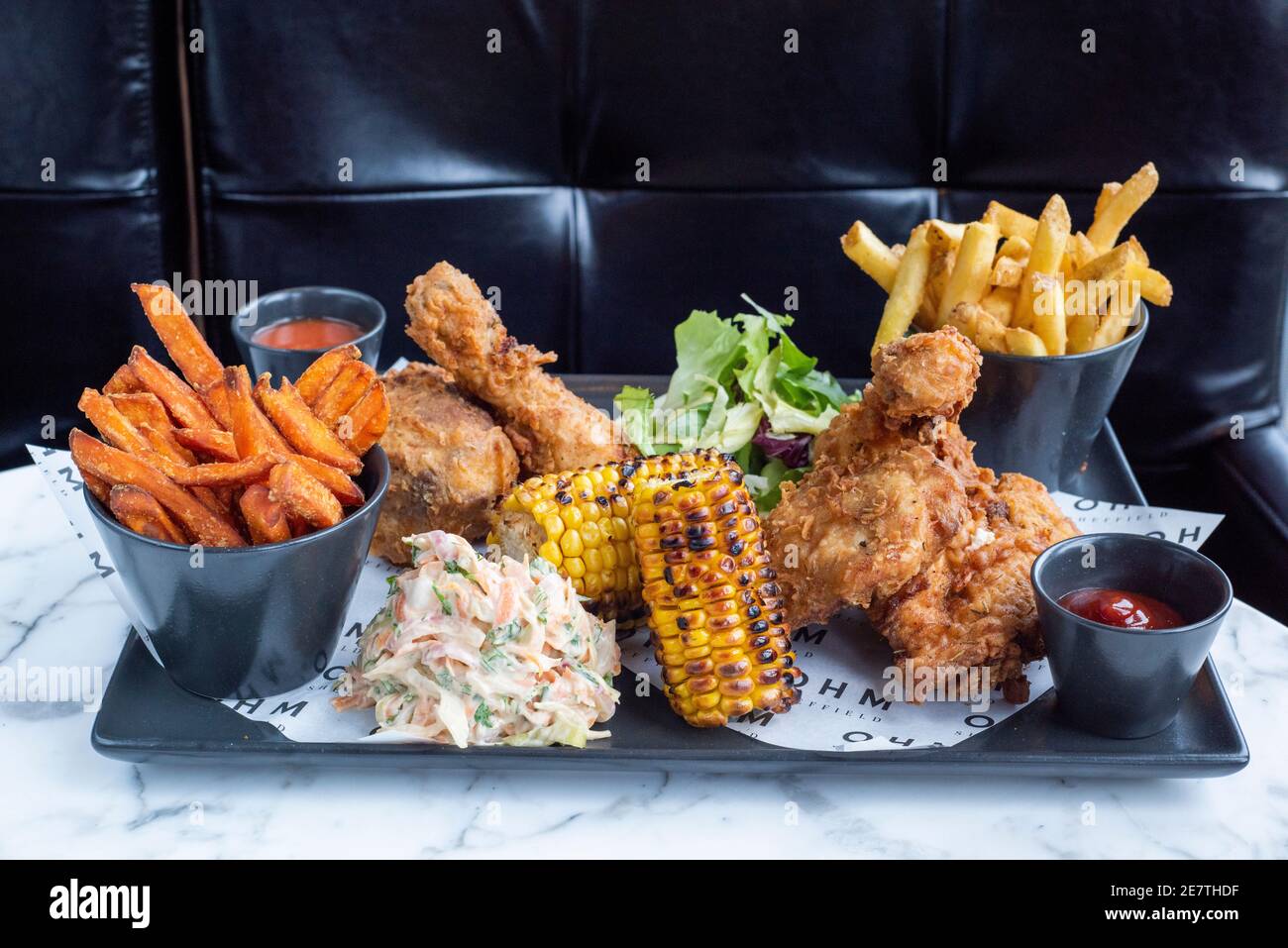 Sheffield, UK - 03 Aug 2017: Southern fried chicken and fries share platter with coleslaw and corn on the cob at OHM, Fitzwilliam Street Stock Photo