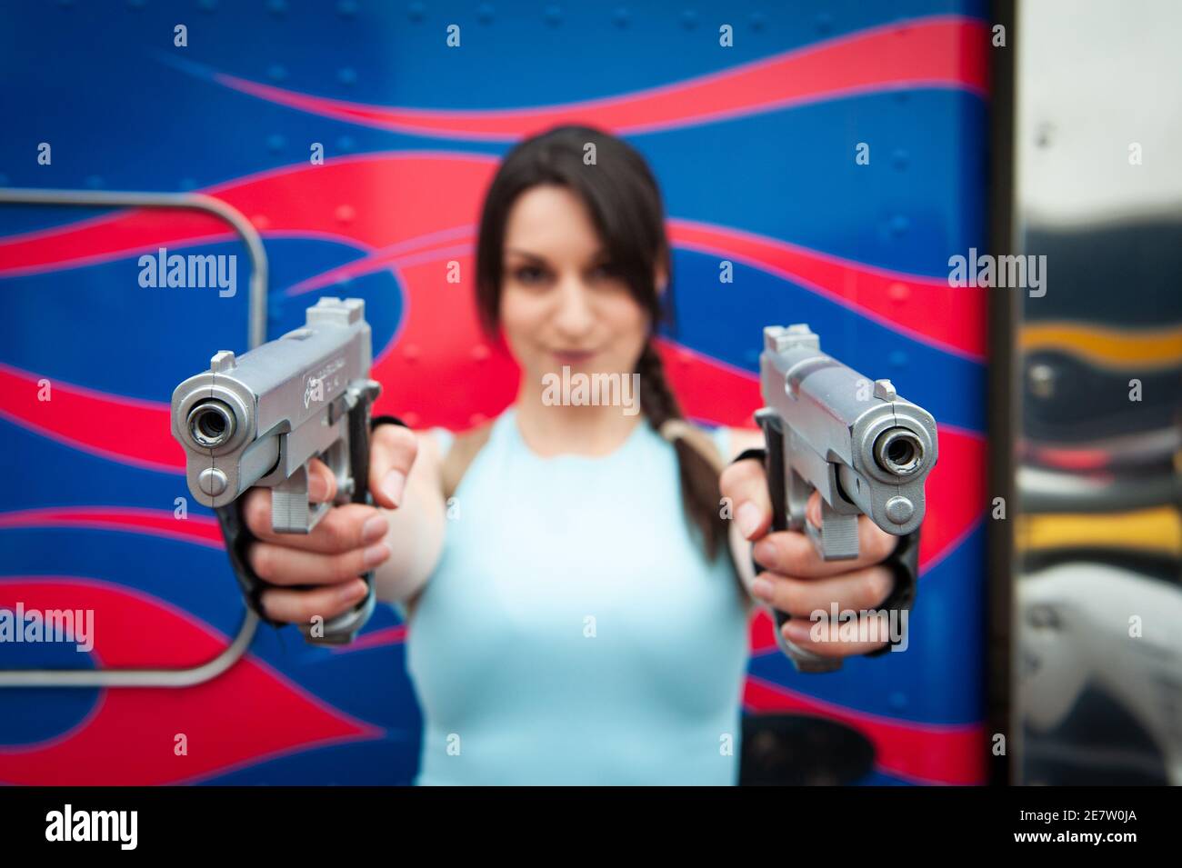 Cos Player dressed as Lara Croft holds 2 guns up to the camera, at London Comic Con, July 2014. Stock Photo