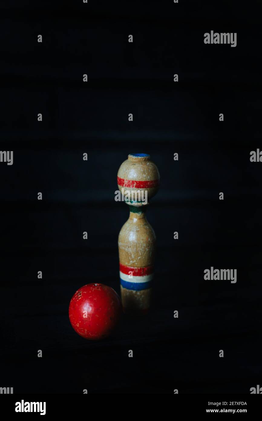 A single wooden bowling pin standing upright beside a red ball Stock Photo