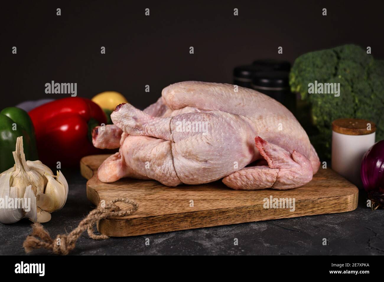 Raw chicken on cutting board surrounded by vegetable ingredients on dark background Stock Photo