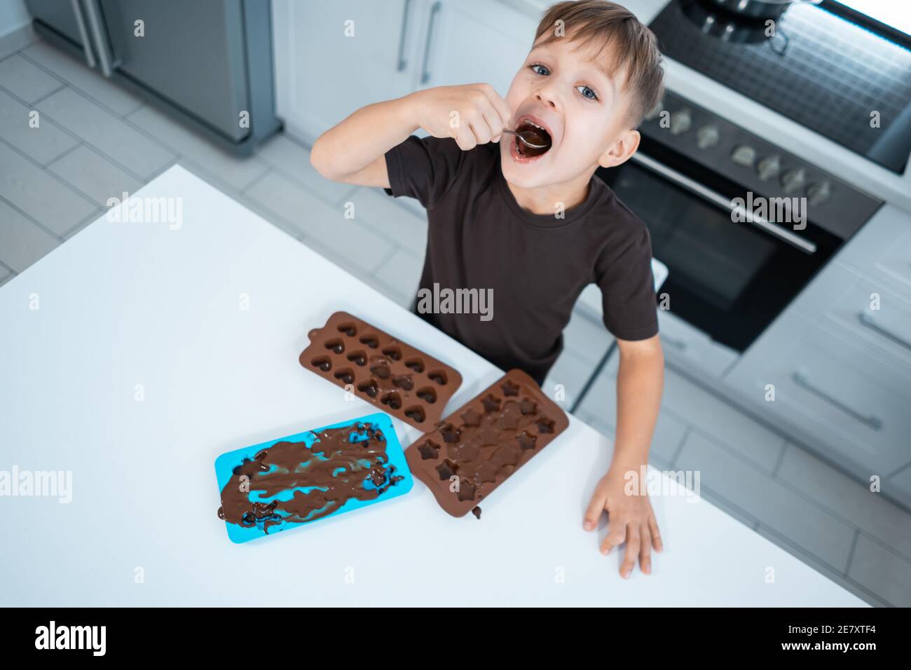 happy kid making chocolate candies or sweets and have fun at home kitchen Stock Photo