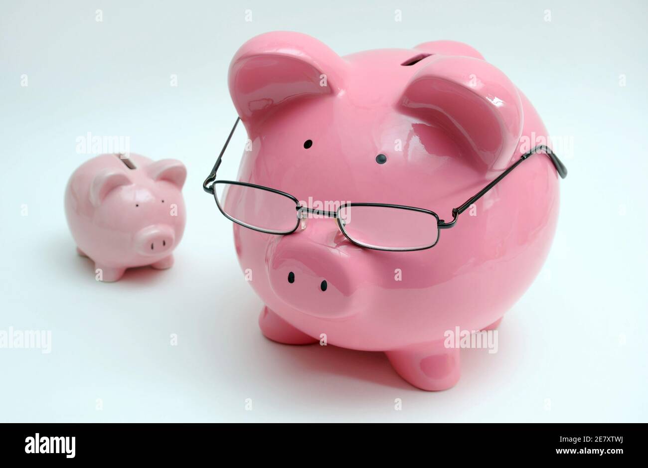 PIGGY BANK WEARING SPECTACLES WITH SMALLER PIGGY BANK RE SAVINGS RETIREMENT PLAN PENSIONS OLD AGE ETC UK Stock Photo