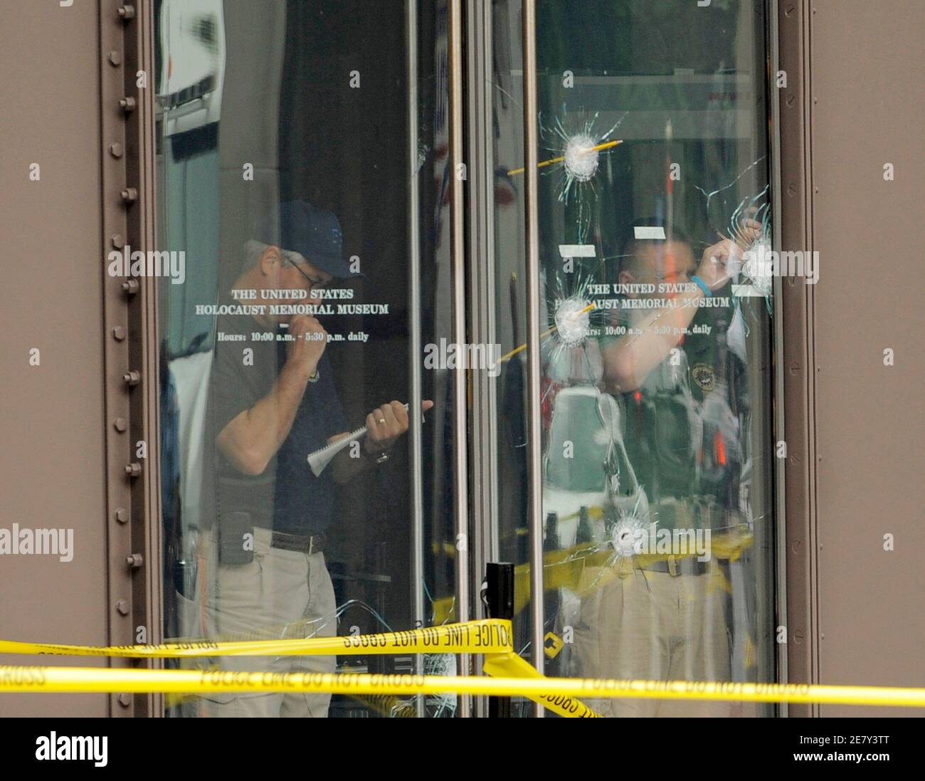 Forensic personnel inspect bullet holes in the glass entry doors at the Holocaust Memorial Museum in Washington, June 11, 2009. An elderly gunman, 88-year old James von Brunn, entered the museum yesterday with a rifle, killing security guard Stephen Tyrone Johns before von Brunn was shot and seriously wounded by other security personnel. The museum was closed today in Johns' memory.     REUTERS/Mike Theiler (UNITED STATES CRIME LAW) Stock Photo