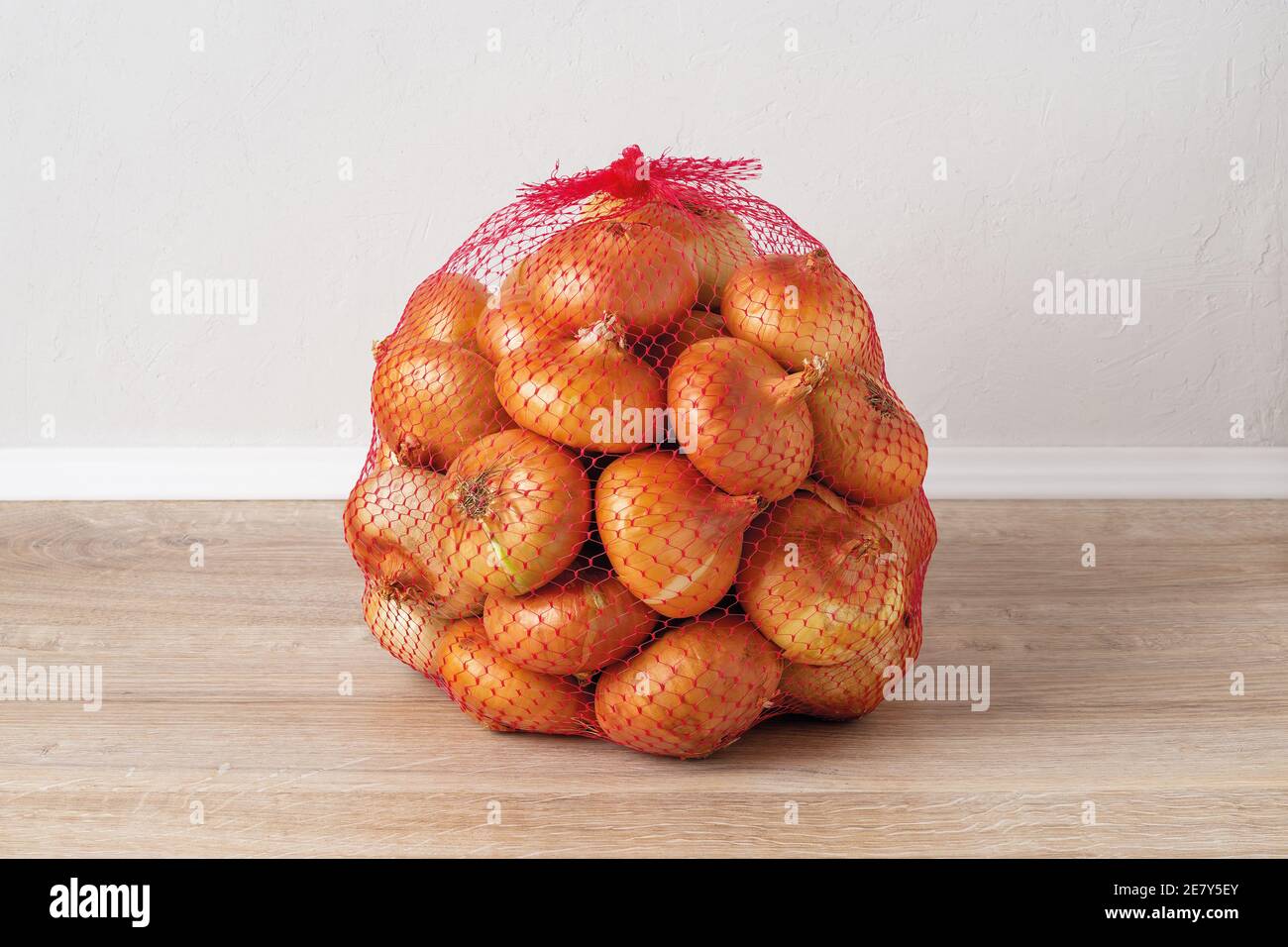 5 kg farm onions in a red pp mesh bag. Polypropylene net sack with 11 lb of  organic onions on a brown floor indoors. Buying fresh vegetables in bulk  Stock Photo - Alamy