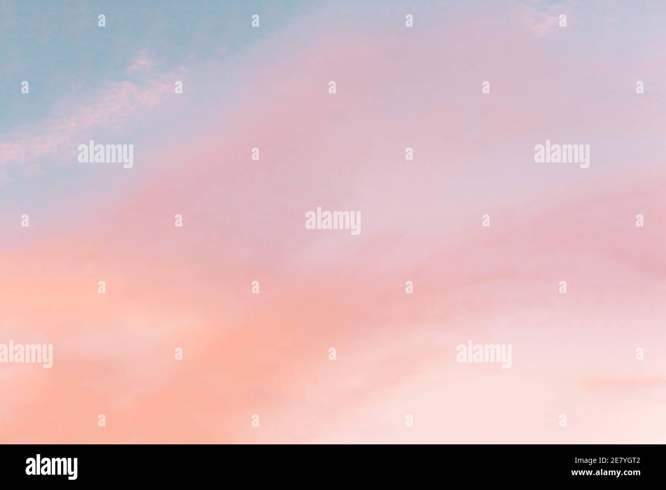 Background formed by a bright pastel authentic sky during sunset. Pink, peach, blue blur backdrop with empty space. Light color gradient transitions. Stock Photo