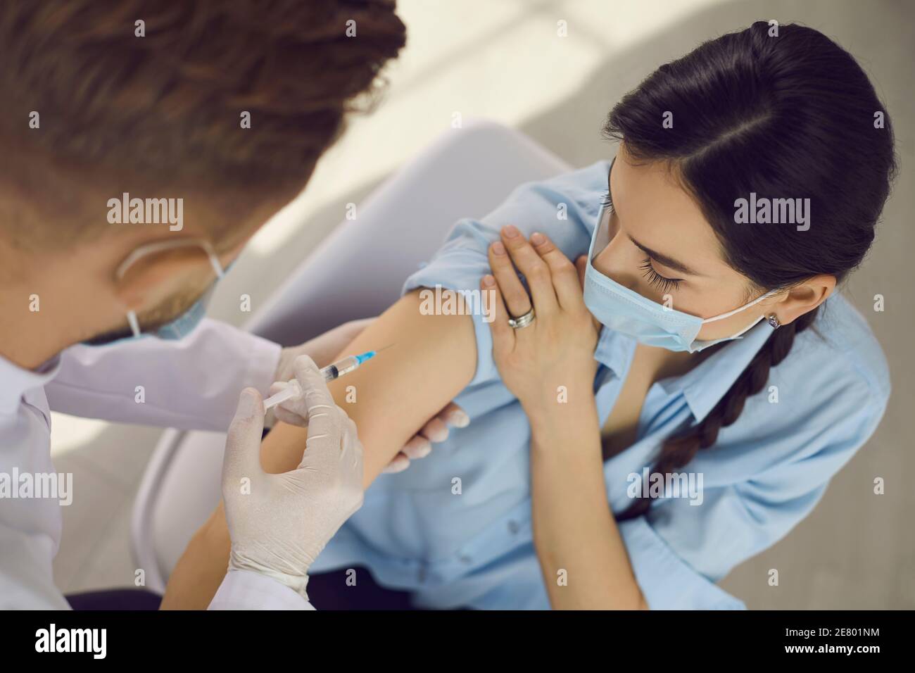 Woman in protective mask looking at doctor medical worker making vaccination injection Stock Photo