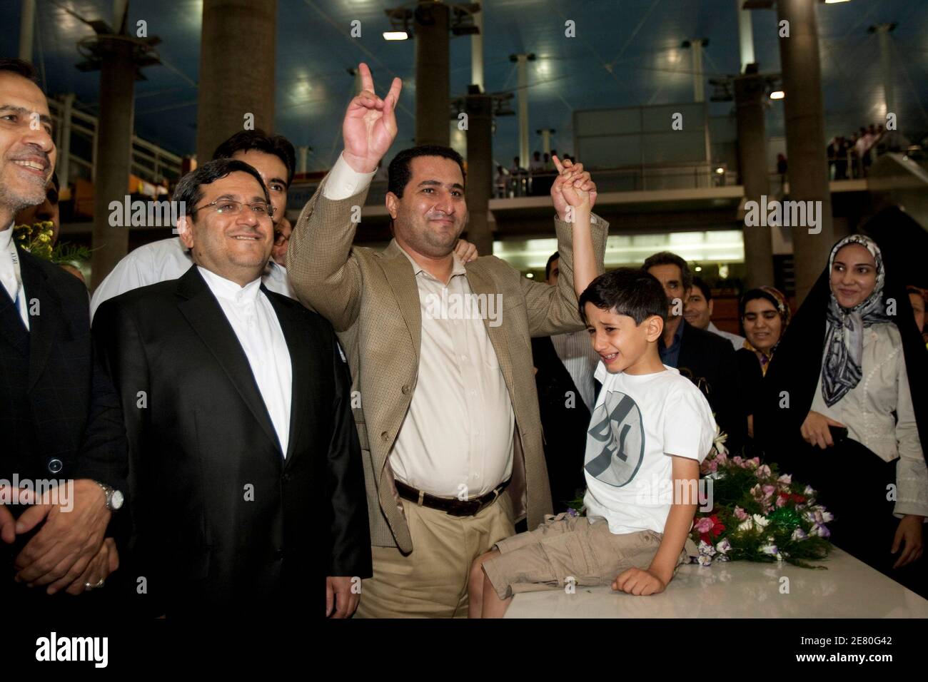 EDITORS' NOTE: Reuters and other foreign media are subject to Iranian restrictions on leaving the office to report, film or take pictures in Tehran.   Iranian scientist Shahram Amiri (C) flashes the victory sign beside his son Amir Hossein as he arrives at the Imam Khomini airport in Tehran July 15, 2010. Amiri, a nuclear scientist who says he was abducted by U.S. agents, thanked Iranian authorities for returning him home on Thursday, the culmination of a murky saga that has underscored deep U.S.-Iranian mistrust.    REUTERS/Raheb Homavandi (IRAN - Tags: POLITICS SCI TECH) Stock Photo
