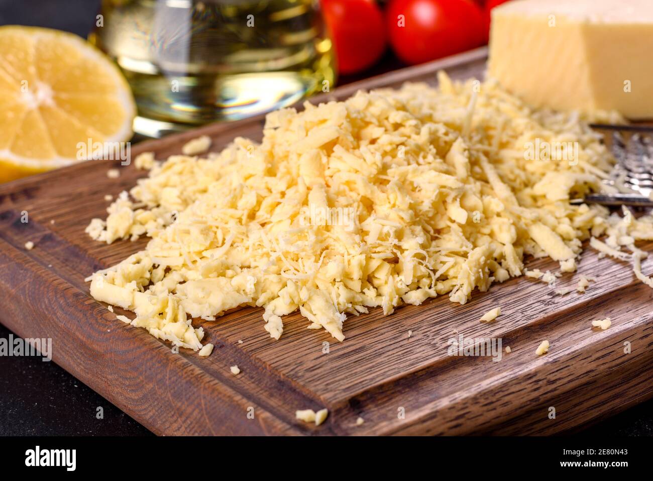 https://c8.alamy.com/comp/2E80N43/fresh-hard-cheese-grated-on-a-large-grater-on-a-wooden-cutting-board-on-a-dark-concrete-background-2E80N43.jpg