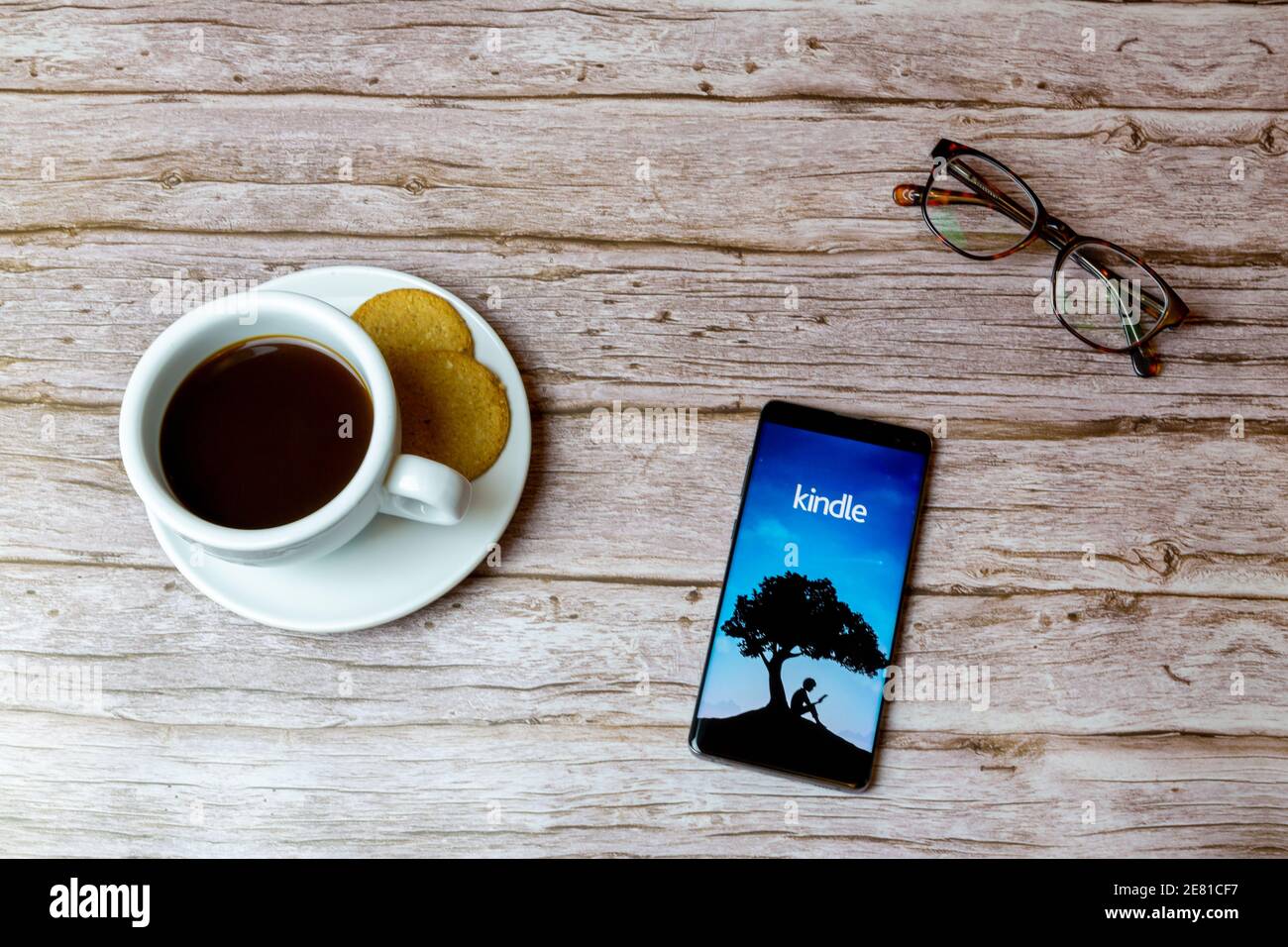 A Mobile phone or cell phone laid on a wooden table with the Amazon Kindle app opening also a coffee and glasses Stock Photo
