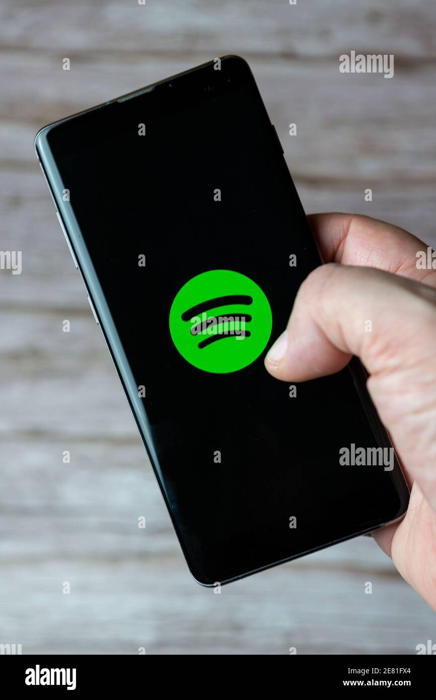 A hand holding a mobile phone or cell phone with the Spotify music app open on screen Stock Photo
