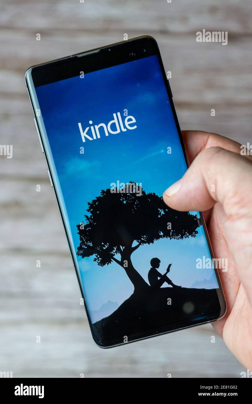 A hand holding a mobile phone or cell phone with the Kindle app open on screen Stock Photo