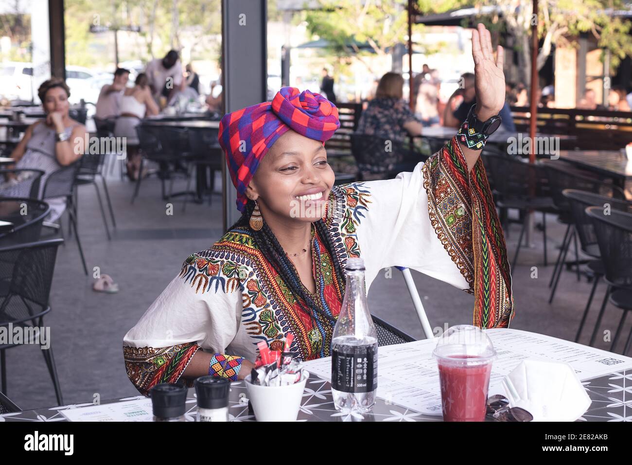 Fashionable African lady wearing a doek or head scarf waving at a friend Stock Photo