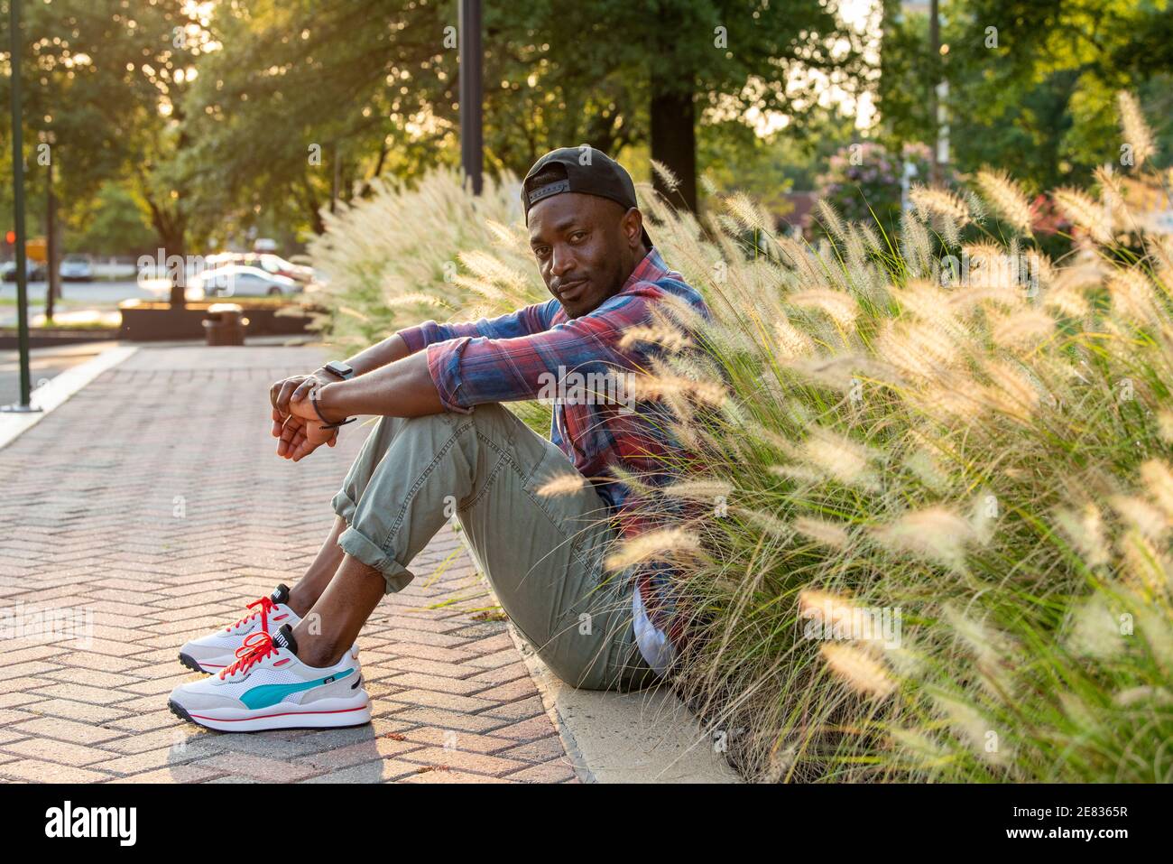 A Black man sits on the curb in an setting. Stock Photo