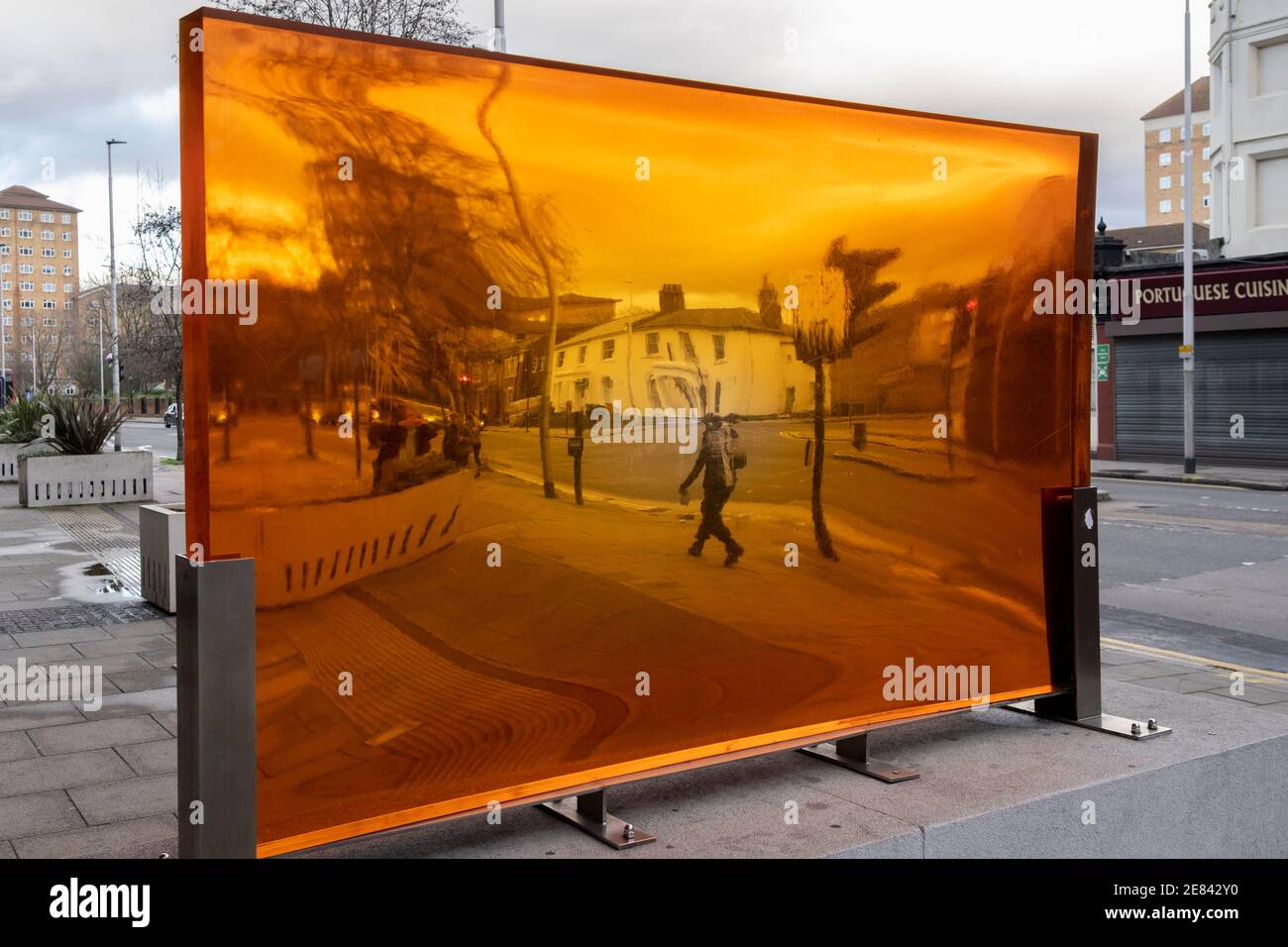 Seen through an orange-coloured prism, a figure walks along a south London street, its distorted perspective and geometry caused by the convex and concave shape of its thick lens, on 29th January 2021, in London, England. Stock Photo