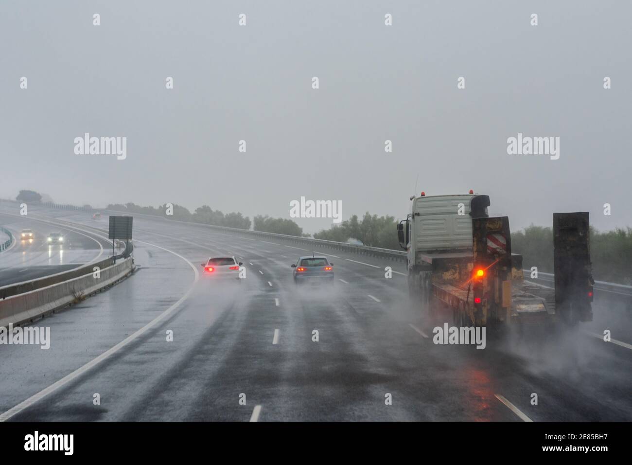 A truck and several cars driving down the highway on a day complicated by the rain. Stock Photo