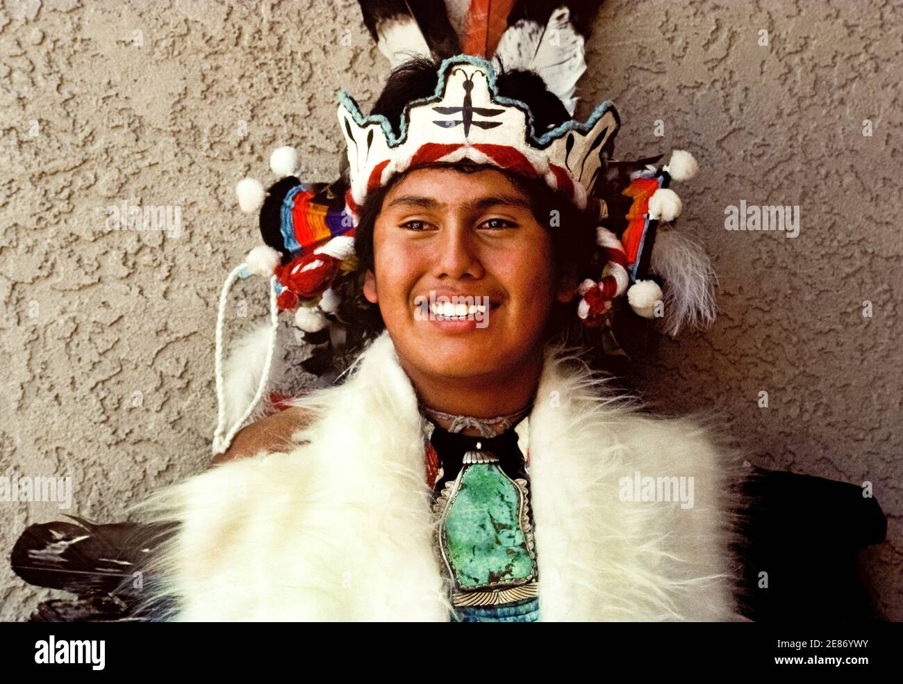 A young Native American man poses in ceremonial dress during a celebration of Indian culture by indigenous peoples of America who gathered to dance, sing and honor the traditions of their ancestors. The powwow was held in Albuquerque, New Mexico, USA, at the Indian Pueblo Cultural Center, a showcase for Pueblo tribes in that southwestern state. The man's elaborate headdress features an image of a dragonfly, a creature seen as a messenger that speaks to the thunder and clouds to bring moisture and blessings to the Pueblo people. Also eye-catching is his necklace with a large turquoise gemstone. Stock Photo