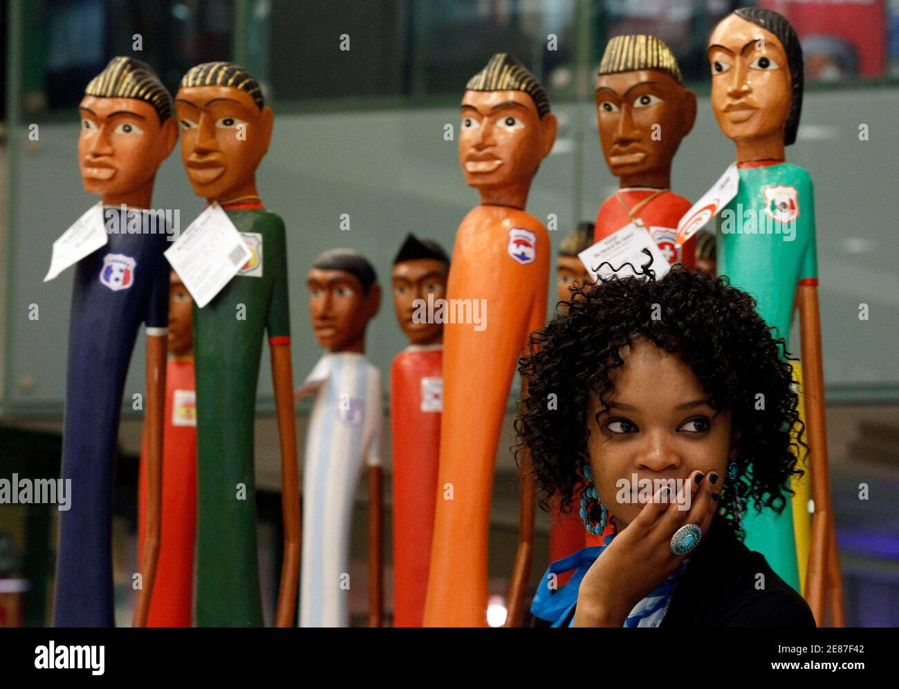 A woman stands in front of the wooden statues representing the various soccer teams taking part in the 2010 World Cup at a shopping centre at Sandton in Johannesburg June 9, 2010. The 2010 World Cup kicks off on June 11 at Soccer City stadium with the match between South Africa and Mexico.  REUTERS/Alessandro Bianchi   (SOUTH AFRICA - Tags: SPORT SOCCER WORLD CUP) Stock Photo