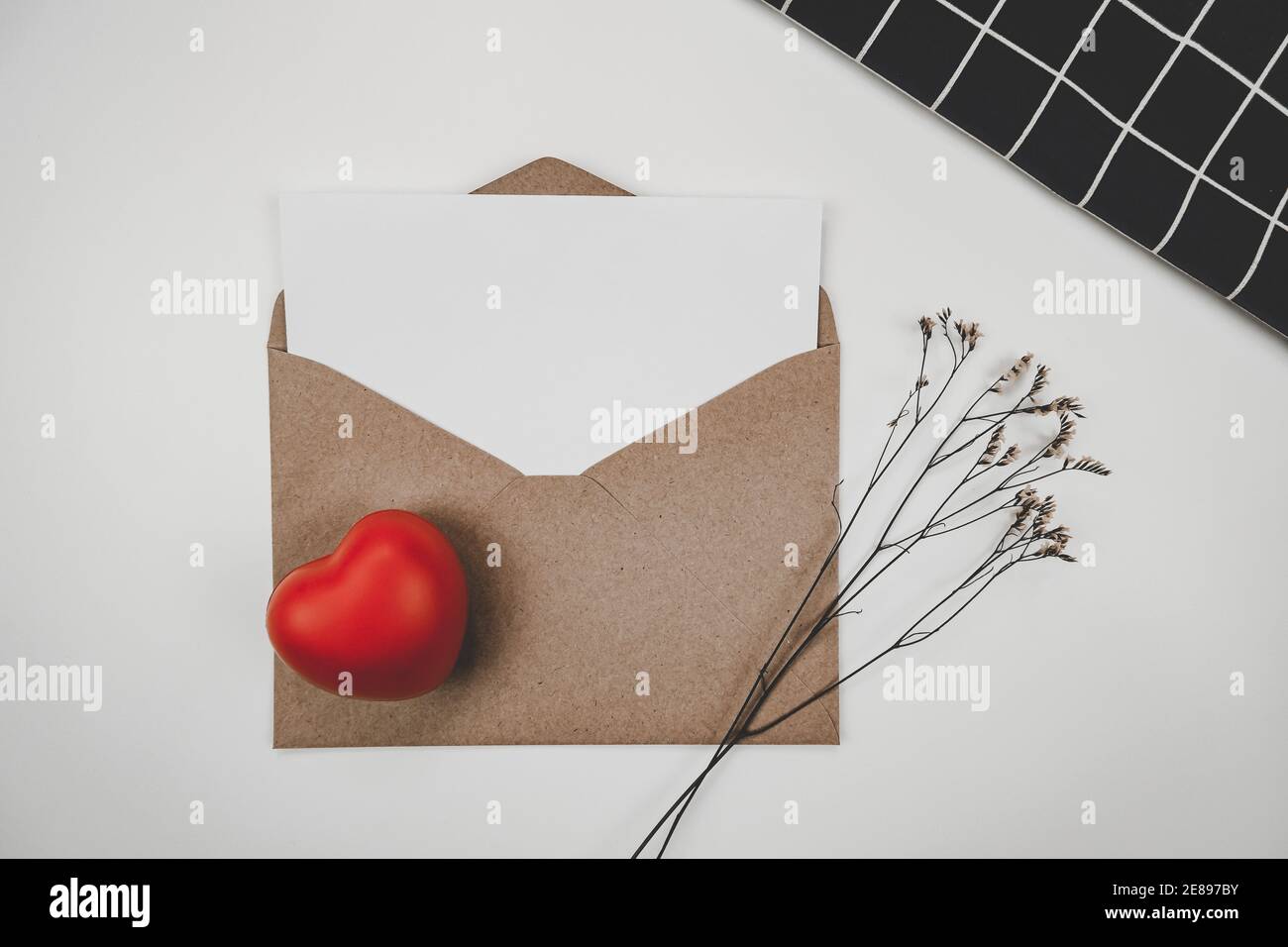 Blank white paper is placed on open brown paper envelope with red heart and Limonium dry flower and black cloth  on white background. Valentine's day Stock Photo