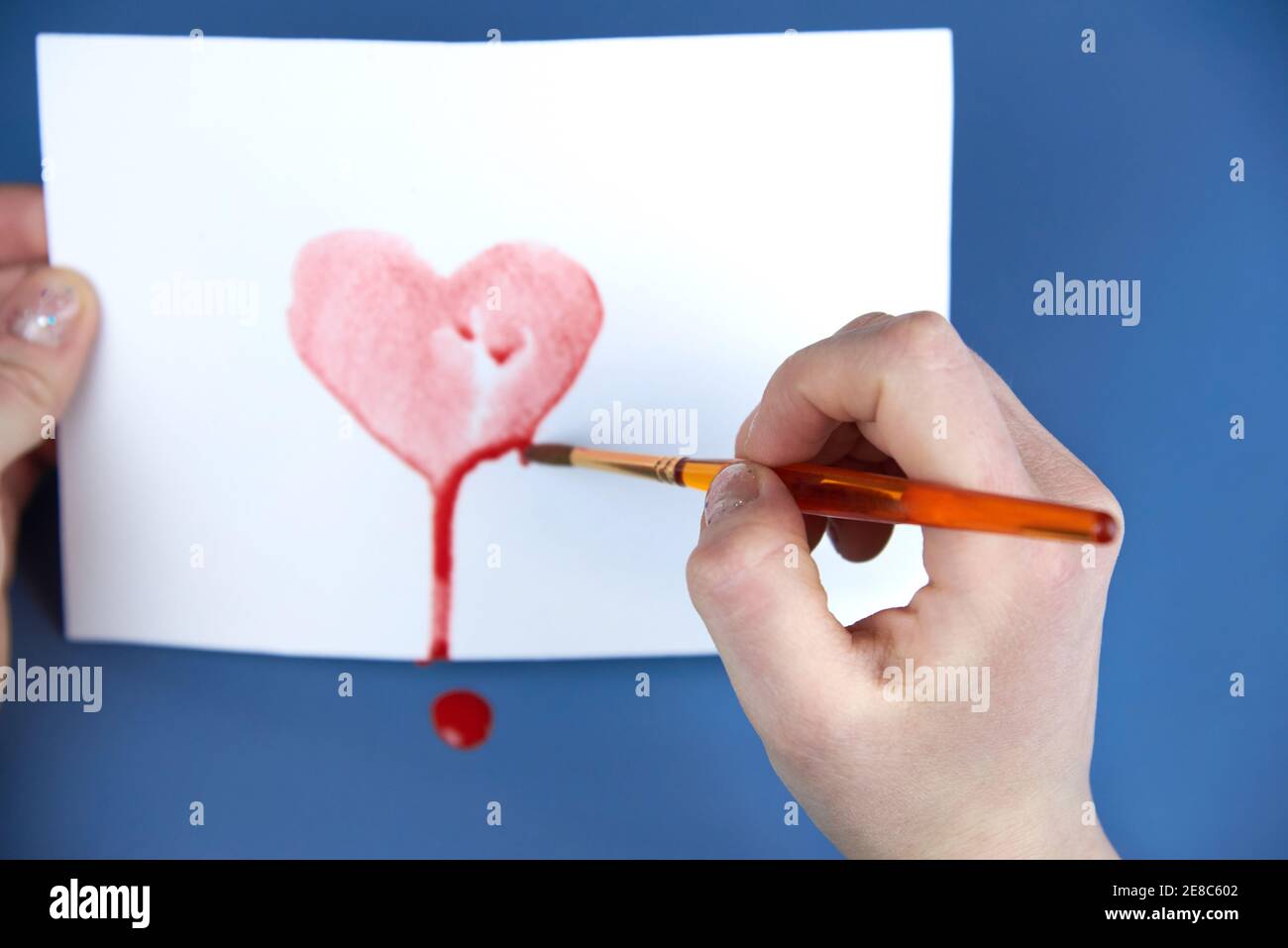 A woman's hand draws a red heart shape in watercolor on white paper ...