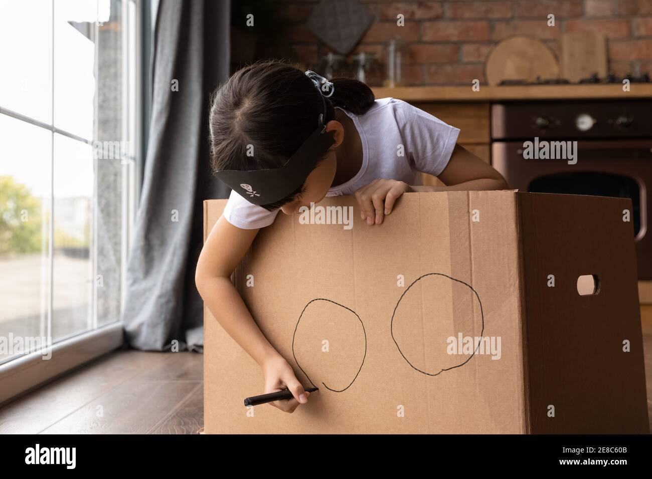 Close up little girl playing pirate, drawing on cardboard box Stock Photo