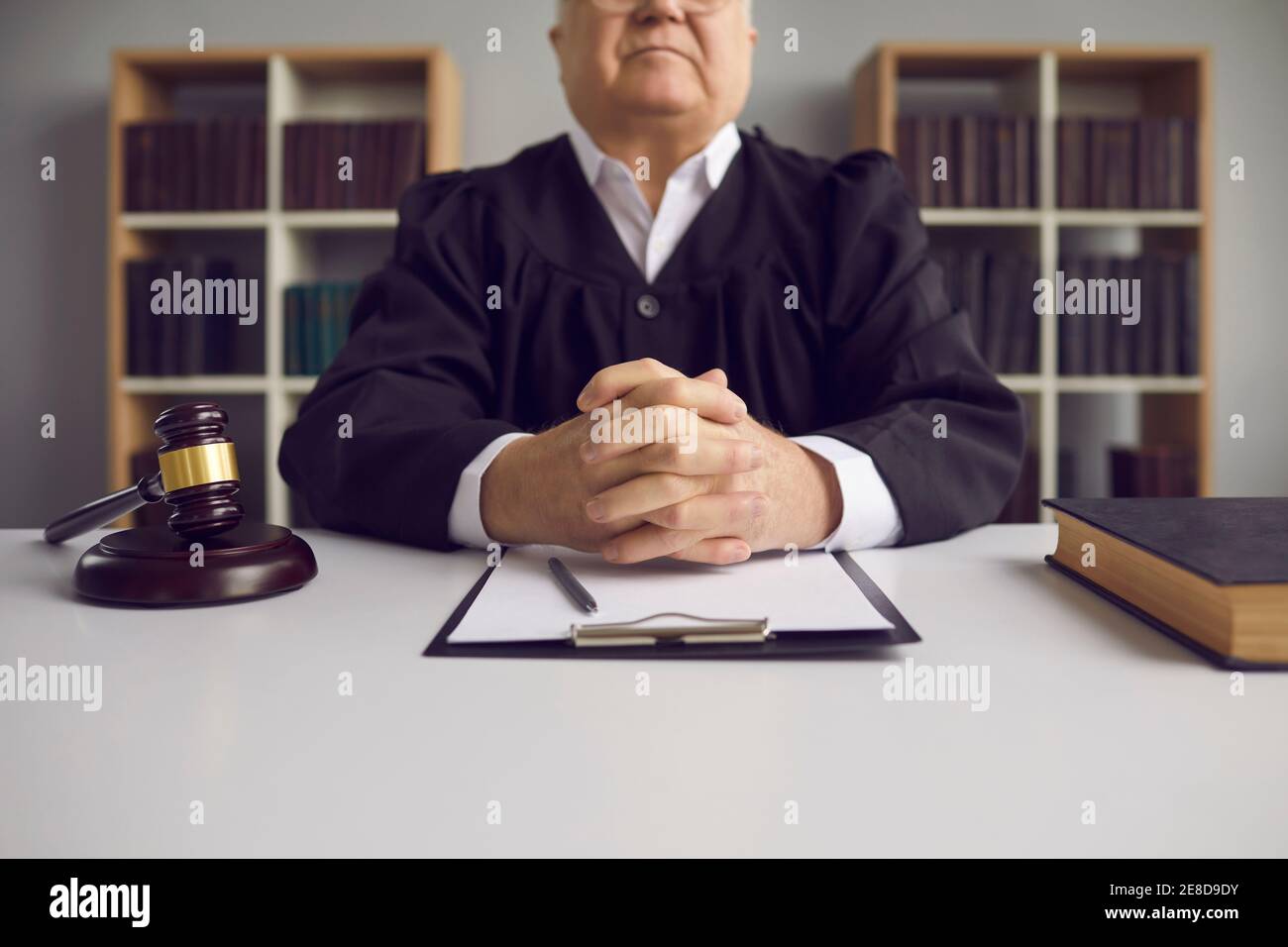 Incorruptible senior judge sitting at table with gavel and case papers in court of law Stock Photo