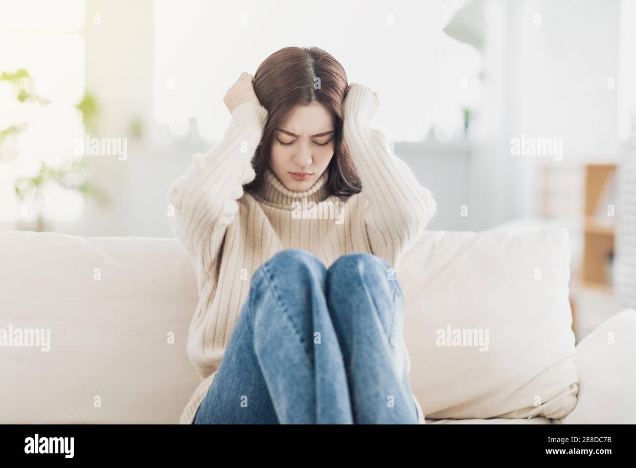 Upset young woman sit on couch at home feel lonely Stock Photo