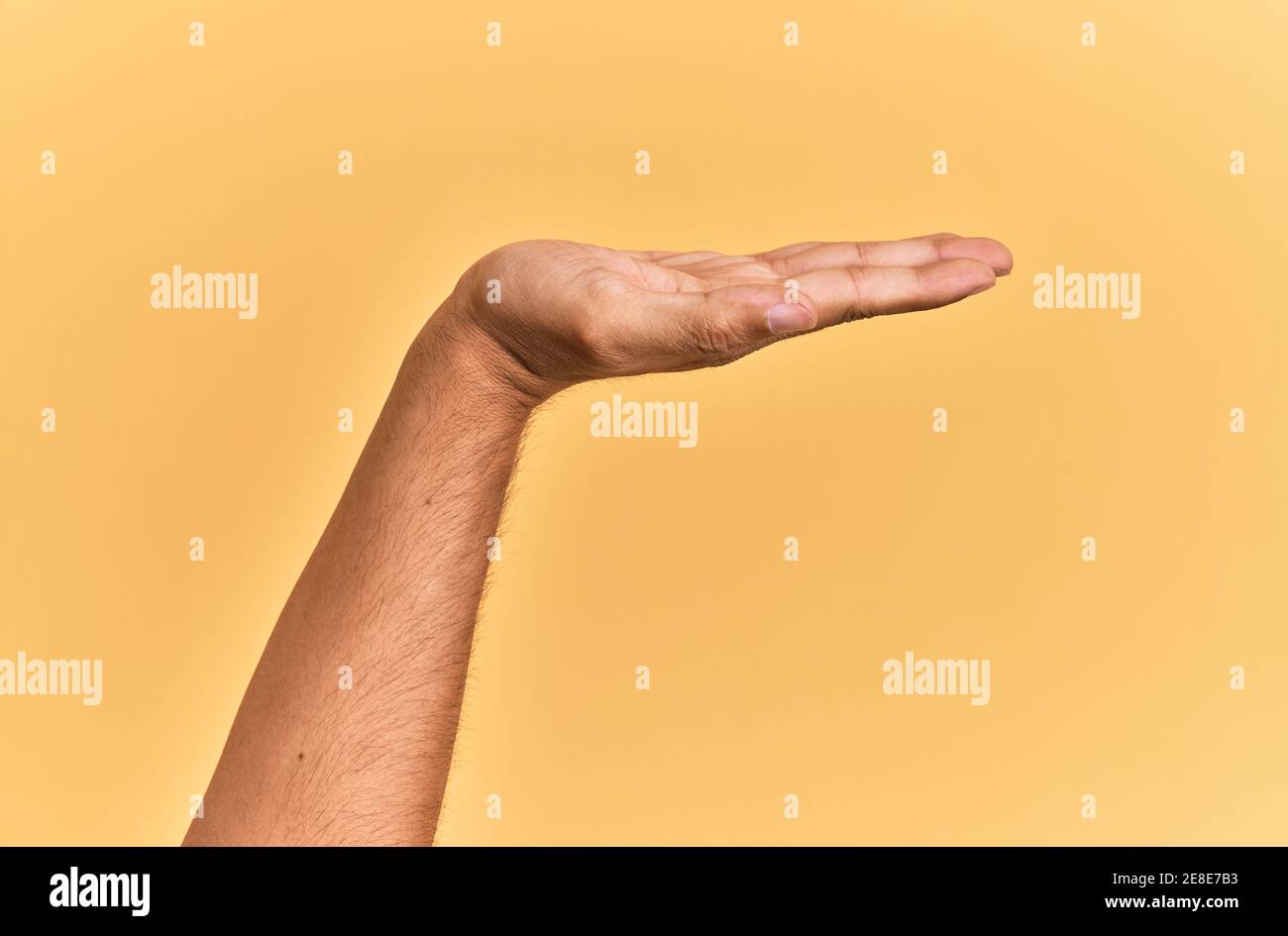 Arm and hand of caucasian man over yellow isolated background with flat palm presenting product, offer and giving gesture, blank copy space Stock Photo