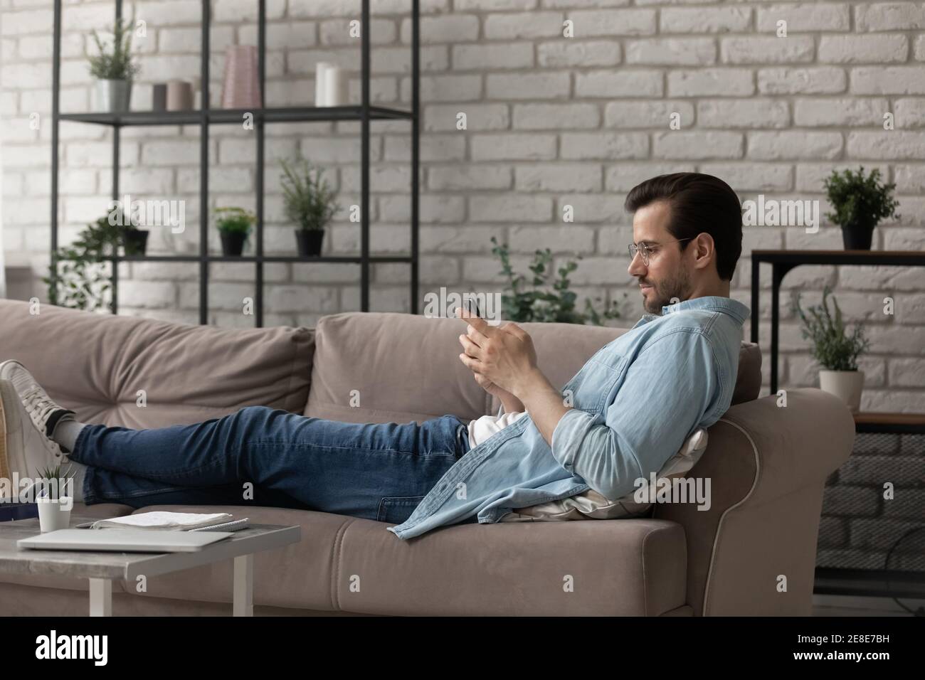 Side view man wearing glasses using phone, lying on couch Stock Photo