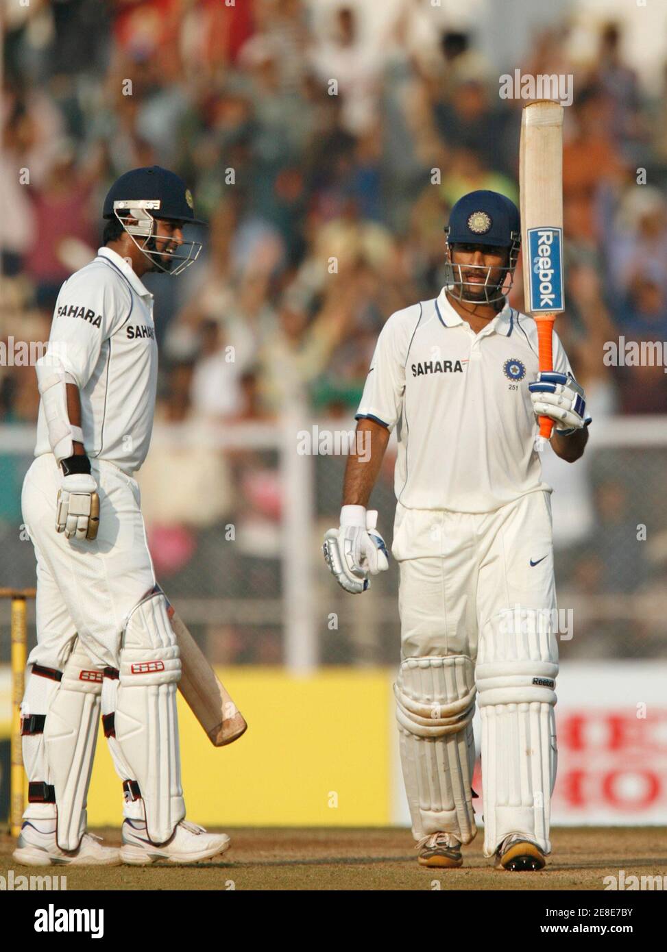 India's captain Mahendra Singh Dhoni (R) celebrates after scoring a  century, as teammate Pragyan Ojha watches, on the third day of their third  test cricket match against Sri Lanka in Mumbai December