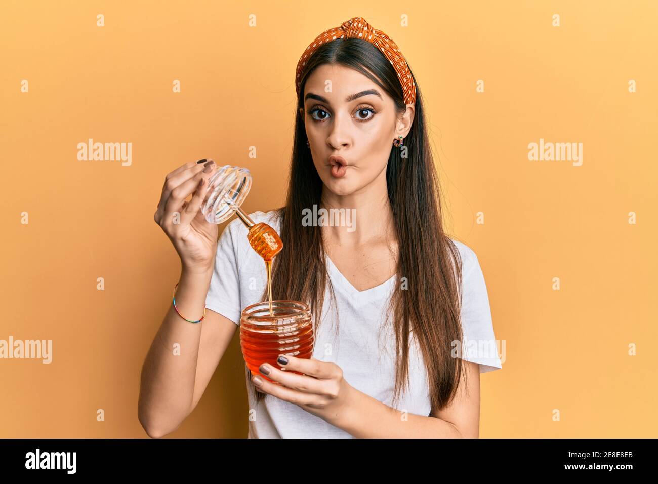 Beautiful brunette young woman holding honey making fish face with mouth and squinting eyes, crazy and comical. Stock Photo