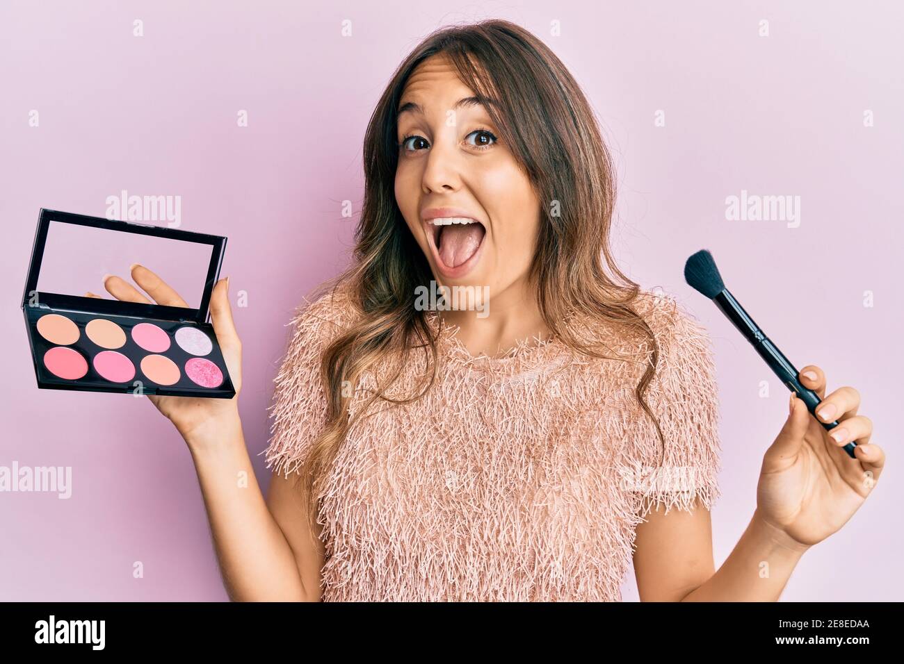 Young woman holding makeup brush and blush celebrating crazy