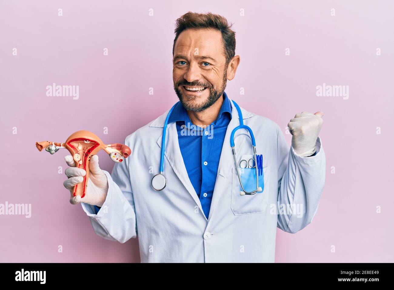Middle age gynecologist man holding anatomical model of female genital organ pointing thumb up to the side smiling happy with open mouth Stock Photo