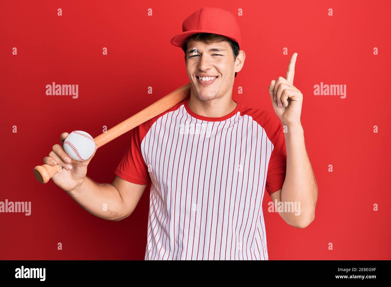 Handsome caucasian man playing baseball holding bat and ball surprised