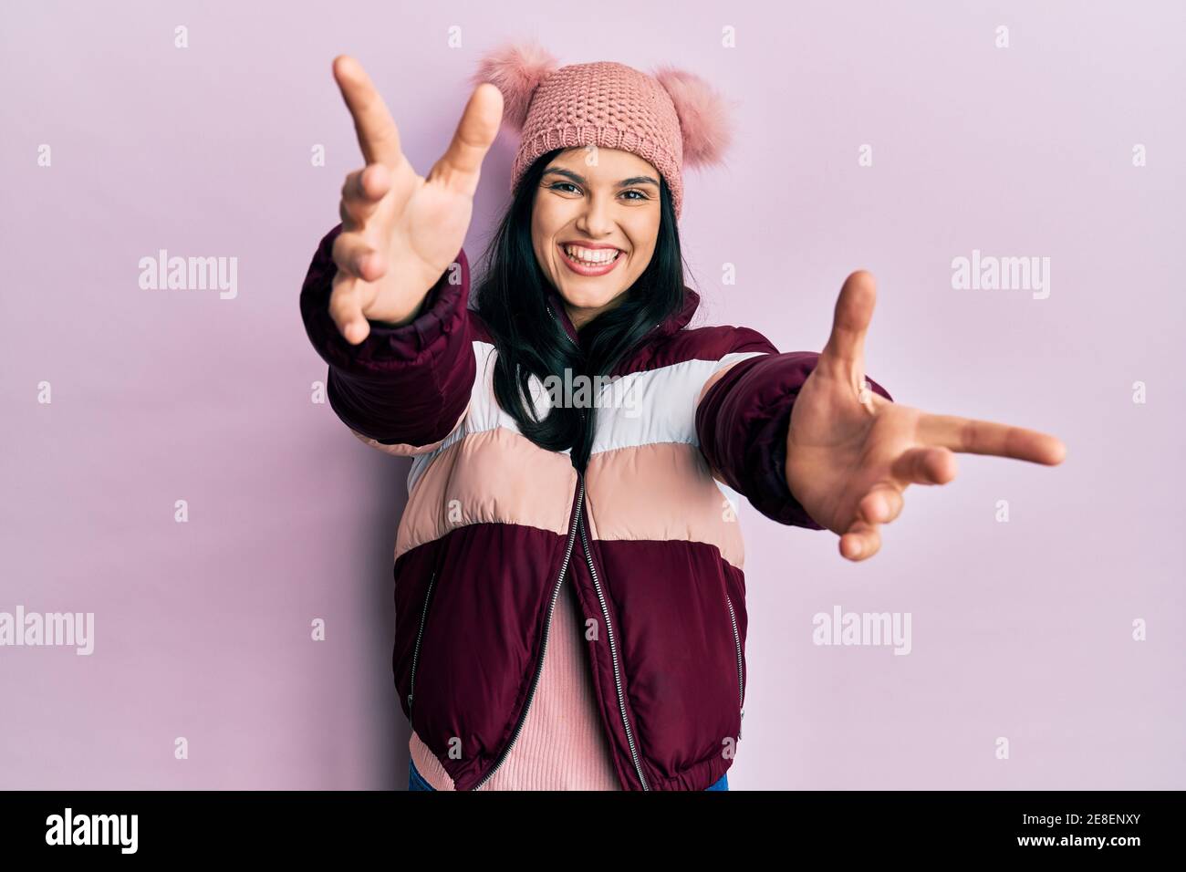 Young hispanic woman wearing wool winter sweater and cap looking at the camera smiling with open arms for hug. cheerful expression embracing happiness Stock Photo
