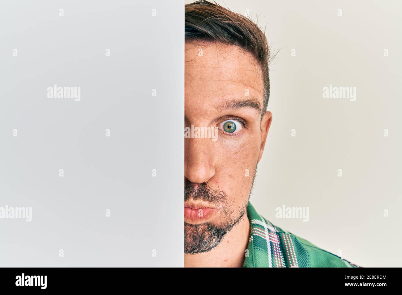 Handsome man with beard holding blank empty banner covering half face puffing cheeks with funny