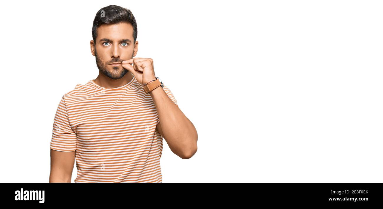 Handsome hispanic man wearing casual clothes mouth and lips shut as zip with fingers. secret and silent, taboo talking Stock Photo