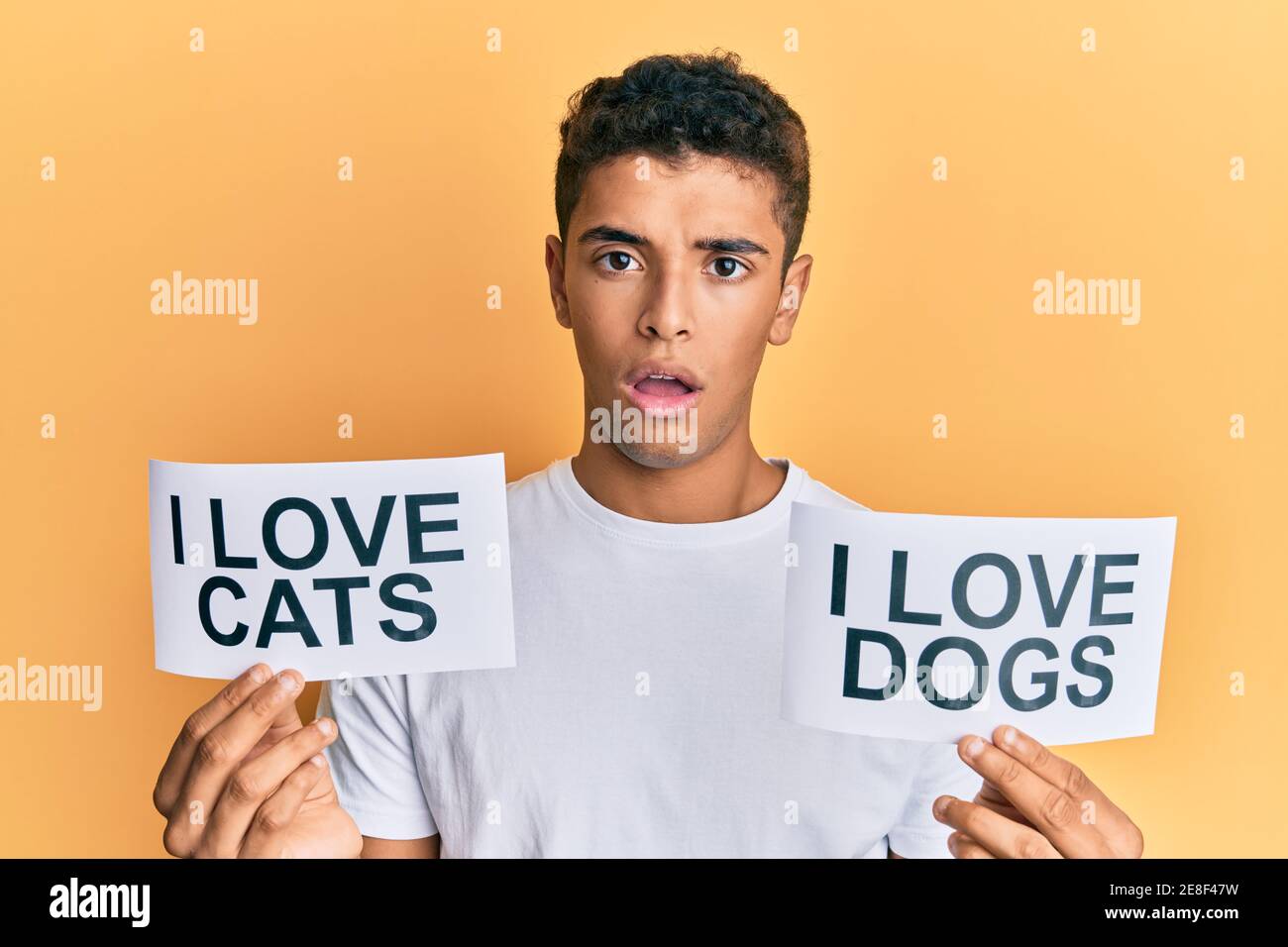 Young handsome african american man holding paper with i love cats and i love dogs phrase in shock face, looking skeptical and sarcastic, surprised wi Stock Photo