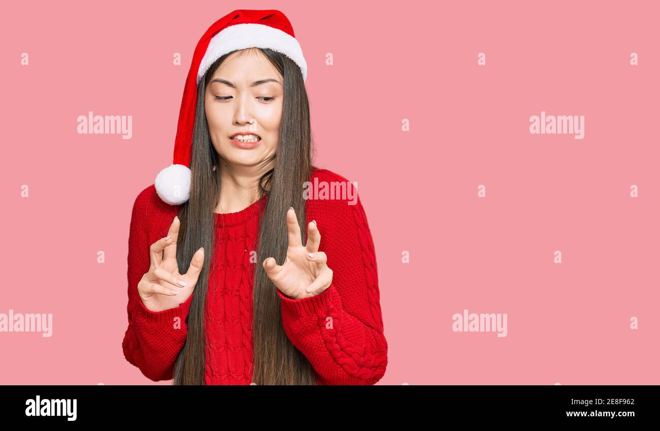 Young chinese woman wearing christmas hat disgusted expression, displeased and fearful doing disgust face because aversion reaction. Stock Photo